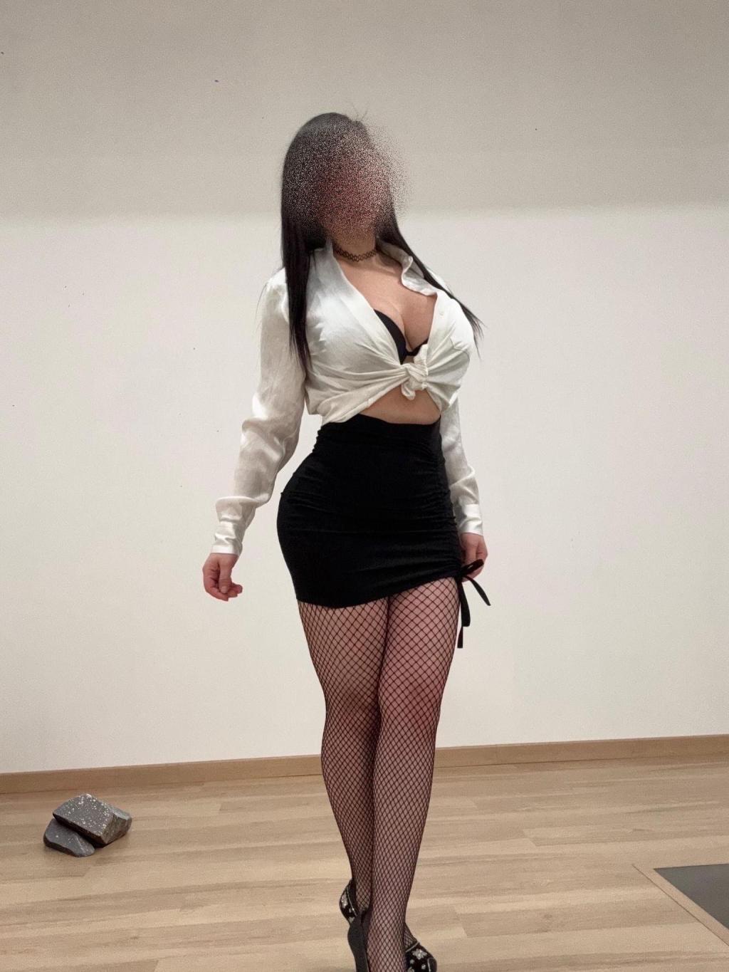 Puta en Córdoba viste una blusa blanca atada al frente y una falda corta negra, con medias de red y tacones.