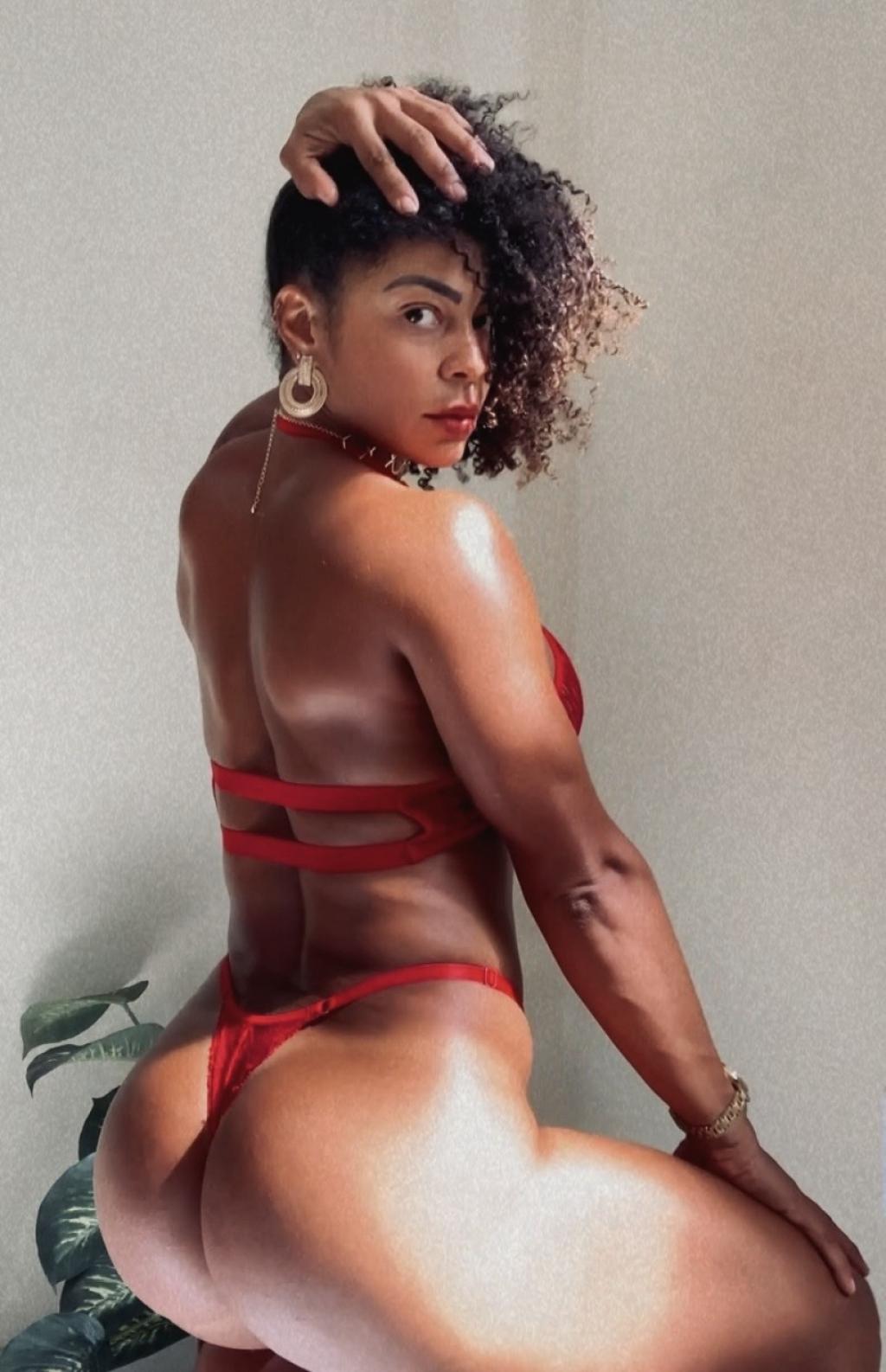 Puta de piel morena y cabello rizado, viste un conjunto de lencería roja en Barcelona, posando de espaldas.