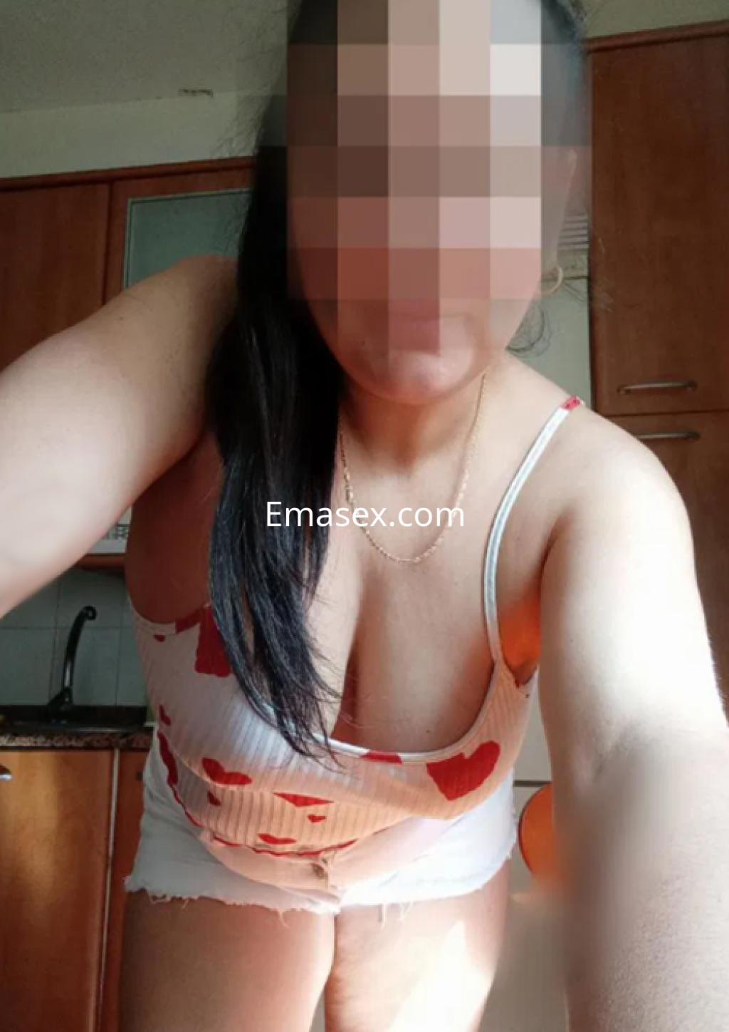 Puta en Pamplona con blusa de tirantes blanca con corazones rojos y short ajustado, sonriendo en una cocina.