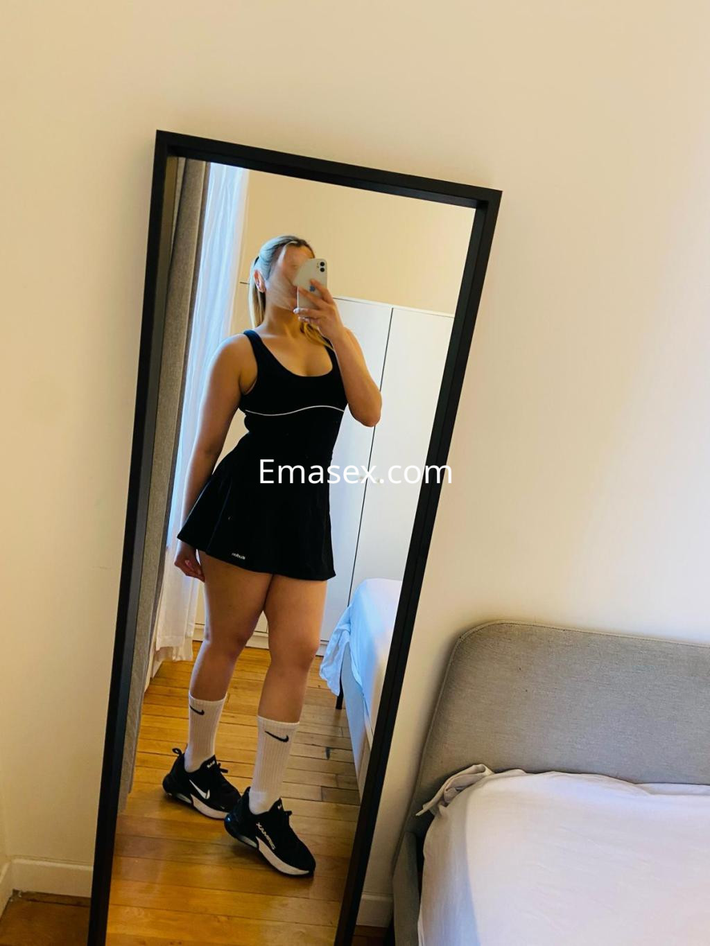 Puta en Málaga luciendo un vestido negro corto y zapatillas deportivas, posando frente a un espejo.
