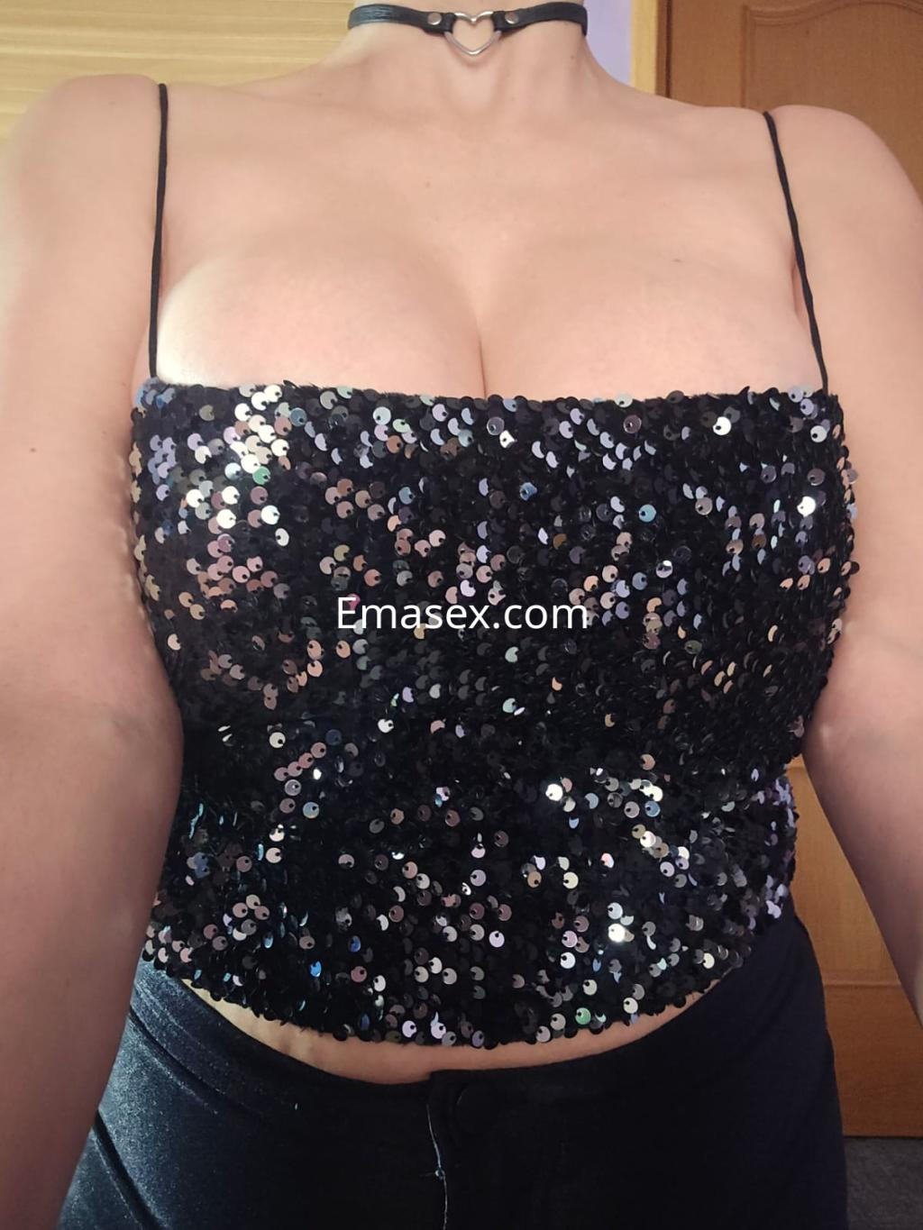 Puta en Gijón luce un top negro brillante con lentejuelas y un collar, mostrando un escote pronunciado.