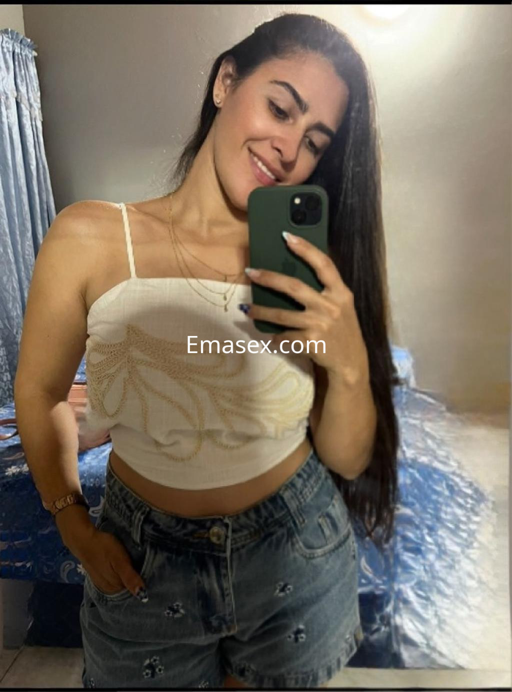 Escort en Santiago sonríe mientras se toma una selfie con blusa blanca y shorts de mezclilla.