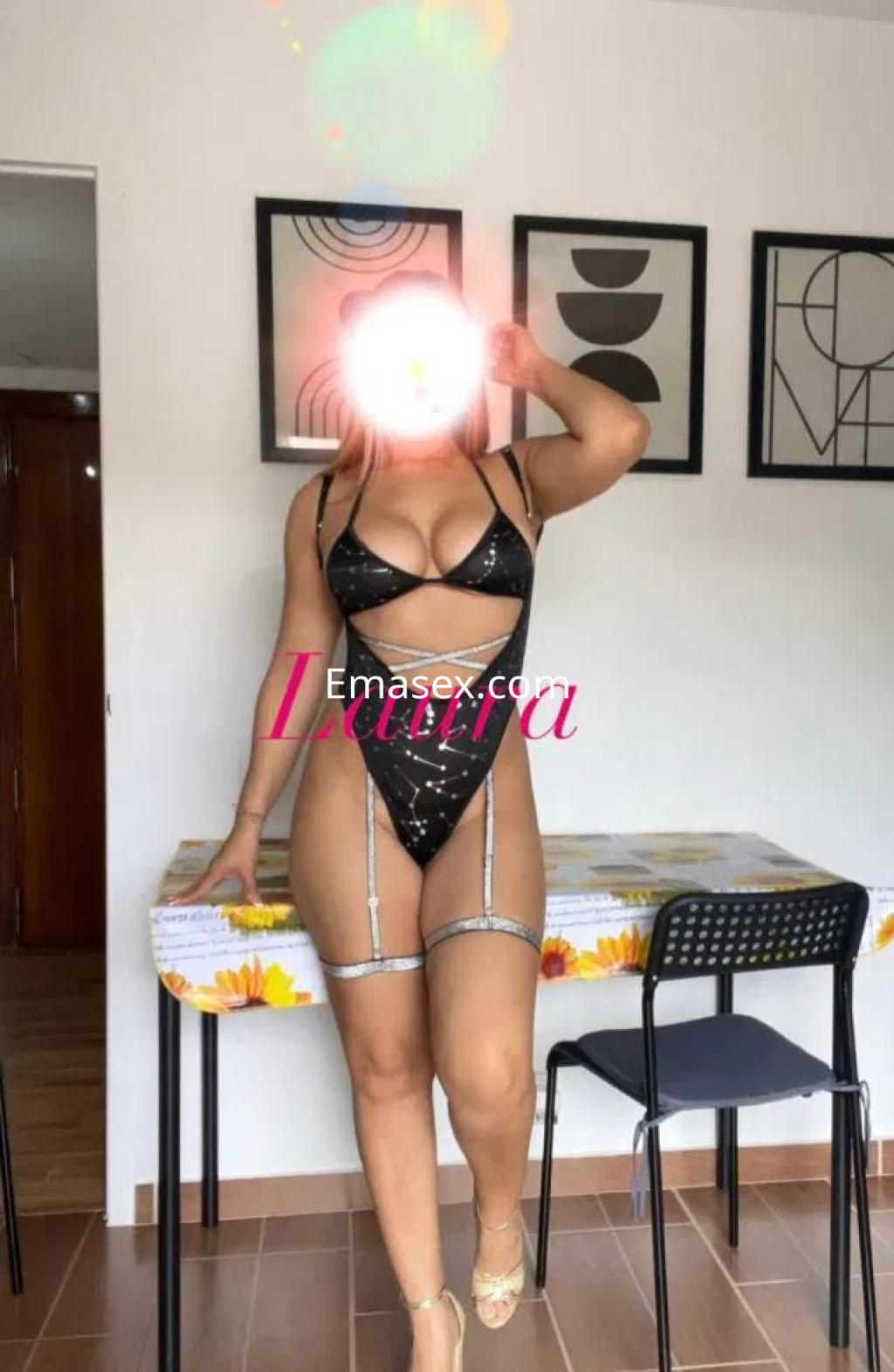 Escort en Albacete viste un conjunto de lencería negra con detalles brillantes, posando en un ambiente moderno.