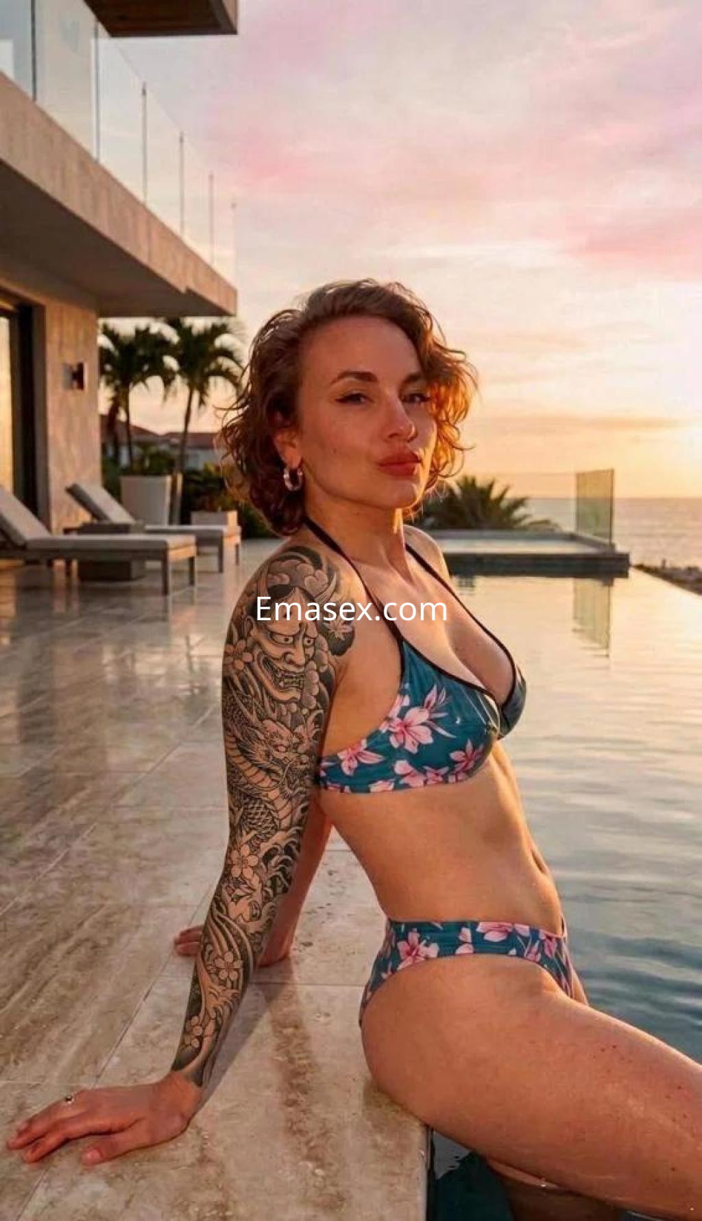 Puta con cabello rizado y tatuajes, posa en bikini floral junto a una piscina en Badajoz al atardecer.