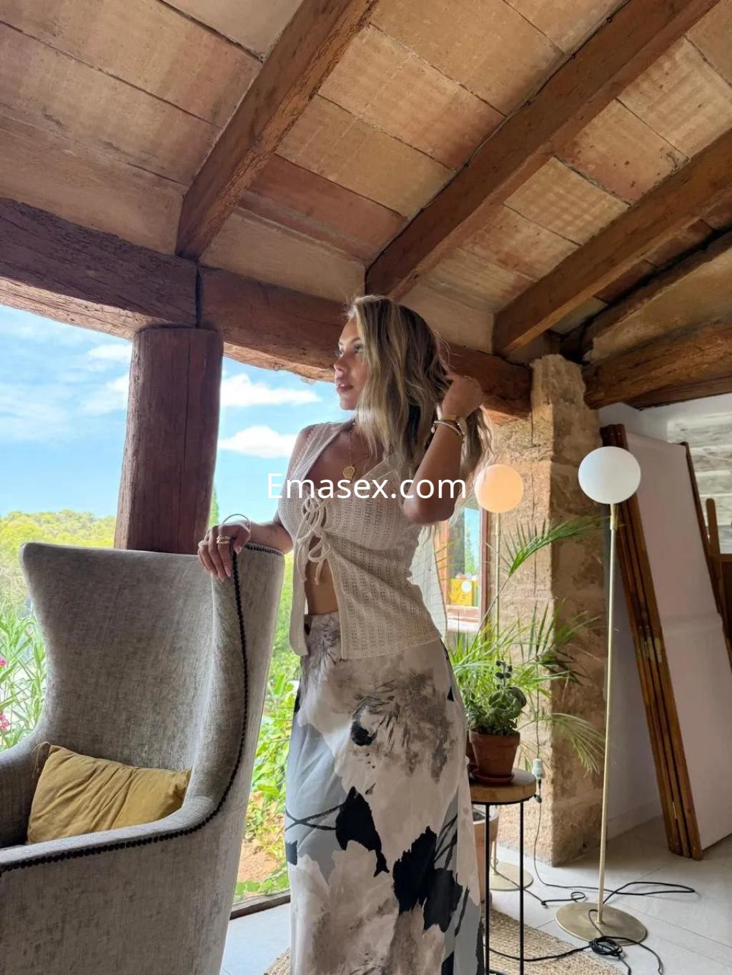 Puta en Coruña, luciendo una blusa blanca y una falda larga con estampado floral, en un ambiente acogedor.