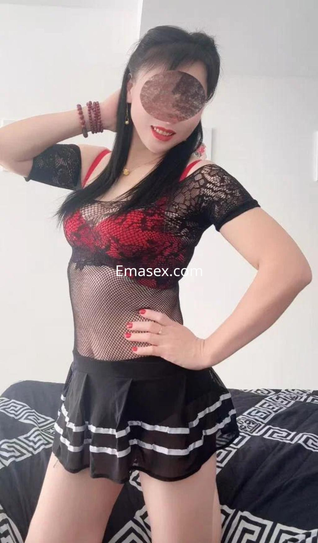 Escort en Gijón luciendo un atrevido conjunto de lencería negra con detalles rojos y una falda corta.