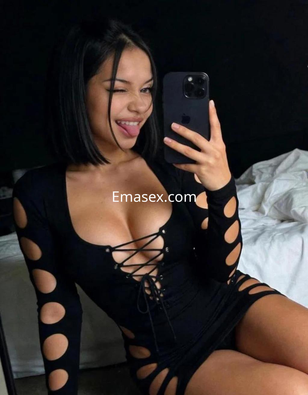 Puta en Badajoz posa con un vestido negro ajustado y recortes, sonriendo mientras se toma una selfie.