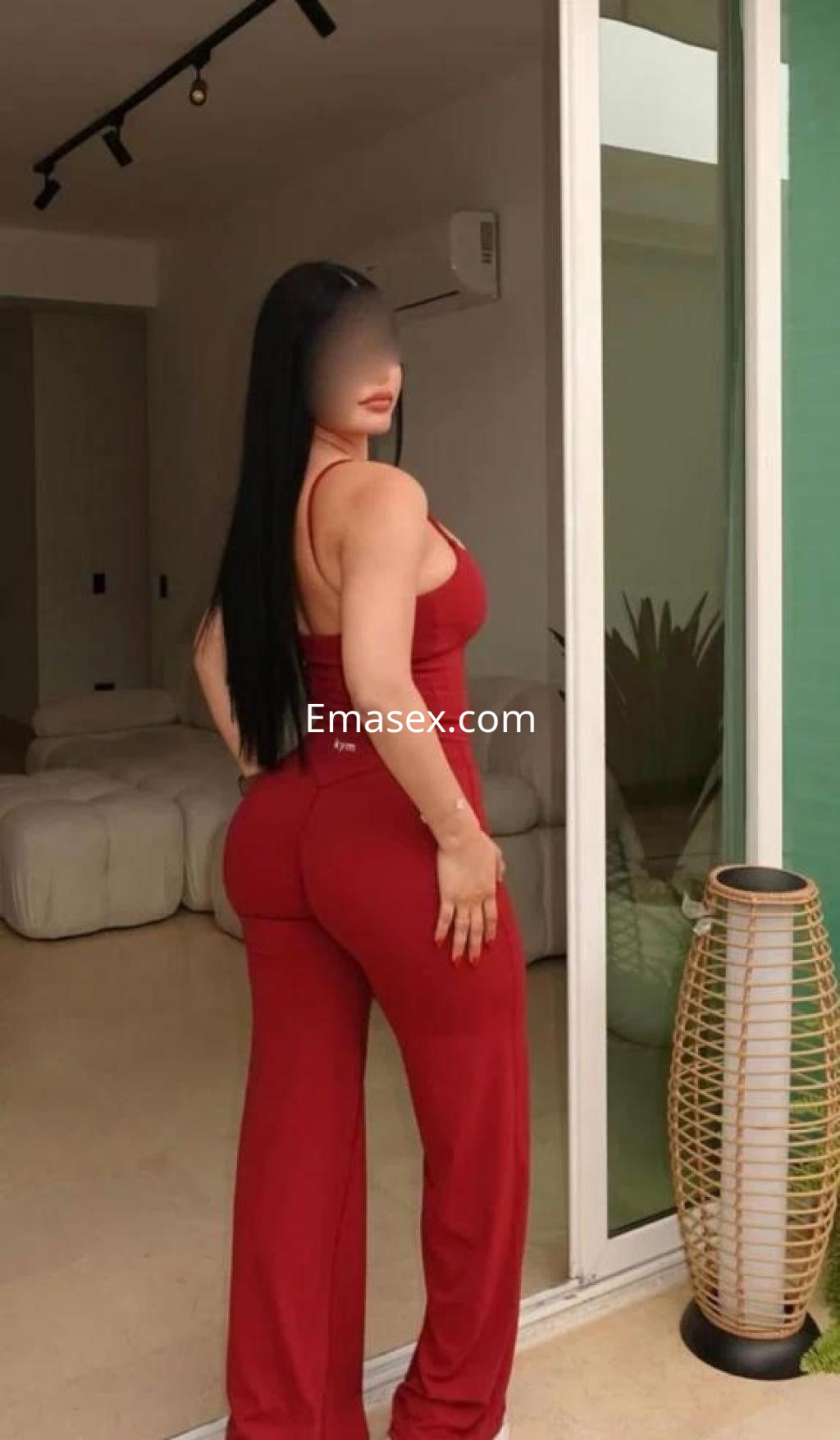 La escort en Zaragoza luce un conjunto rojo ajustado mientras se posa de espaldas, mostrando su larga cabellera negra.