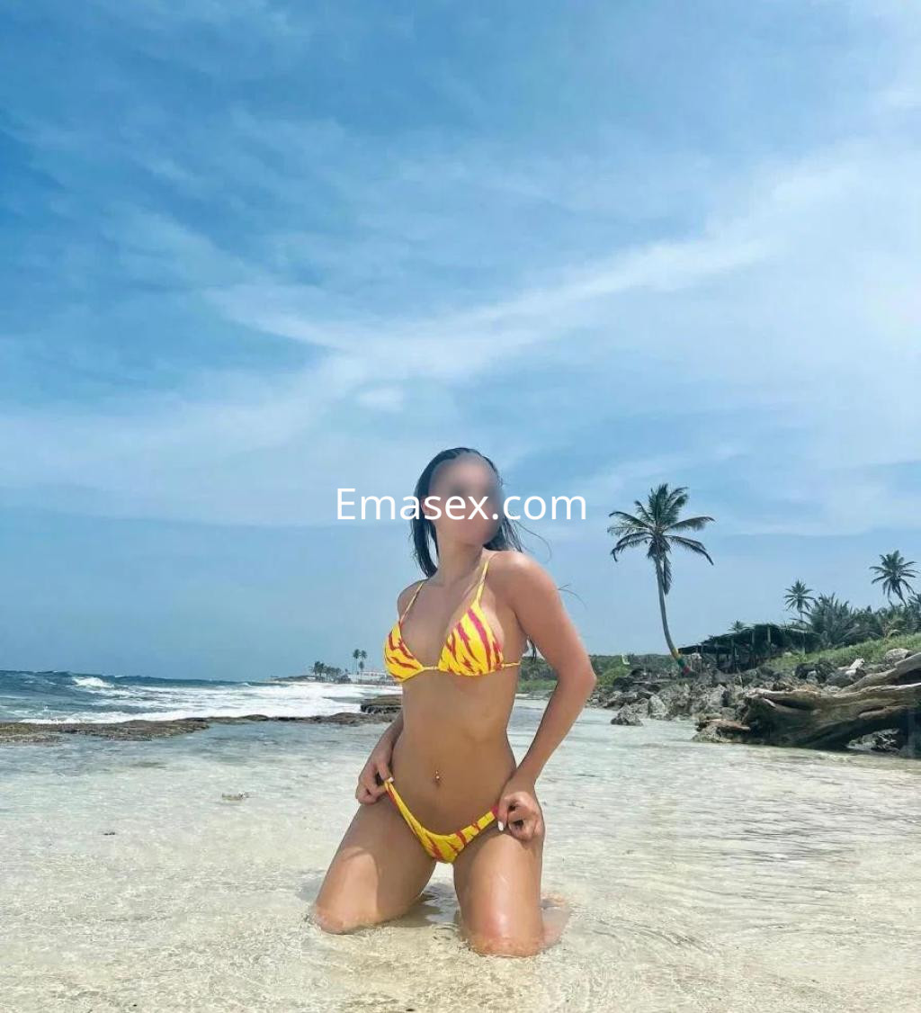 La puta está de rodillas en la orilla del mar en Coruña, luciendo un bikini amarillo con rayas.