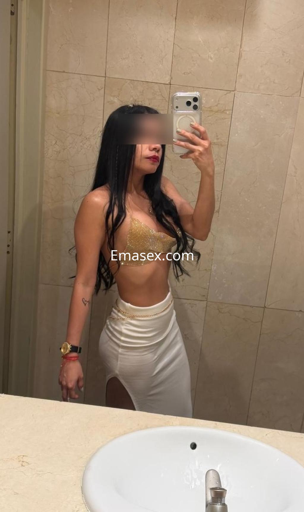 Escort en Almería luciendo un top dorado y una falda blanca ajustada, posando en un espejo.