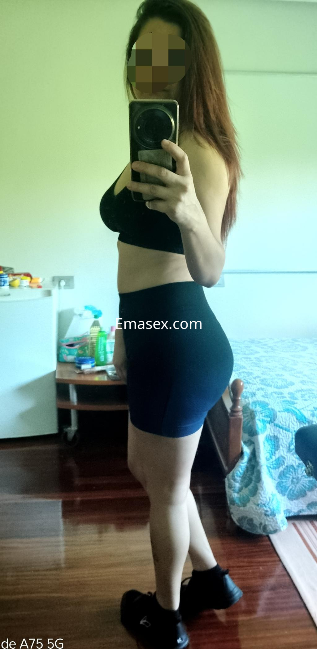 Escort en León posando de perfil con top negro y shorts ajustados, mostrando un ambiente interior sencillo.