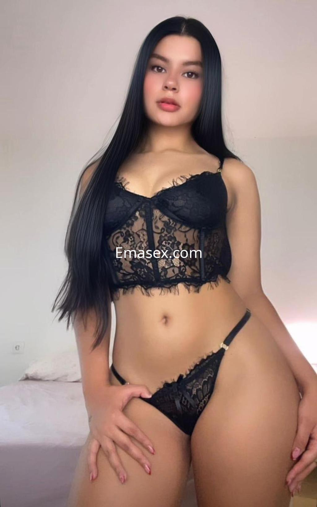 Puta en Gijón, luciendo un conjunto de lencería negra con encaje, cabello lacio y una pose seductora.