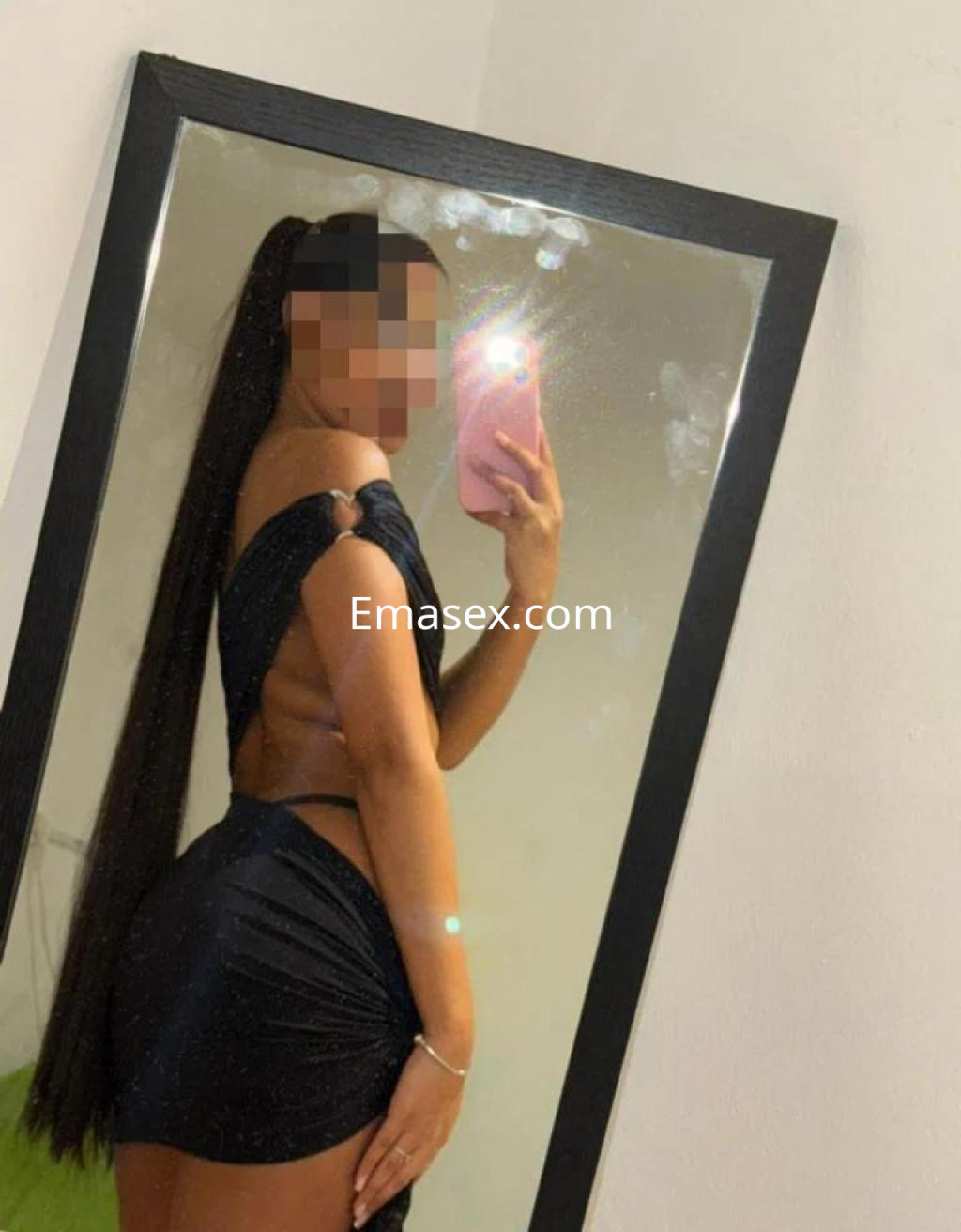 La escort en Barcelona se muestra de perfil frente a un espejo, luciendo un vestido negro ajustado y con el cabello largo.