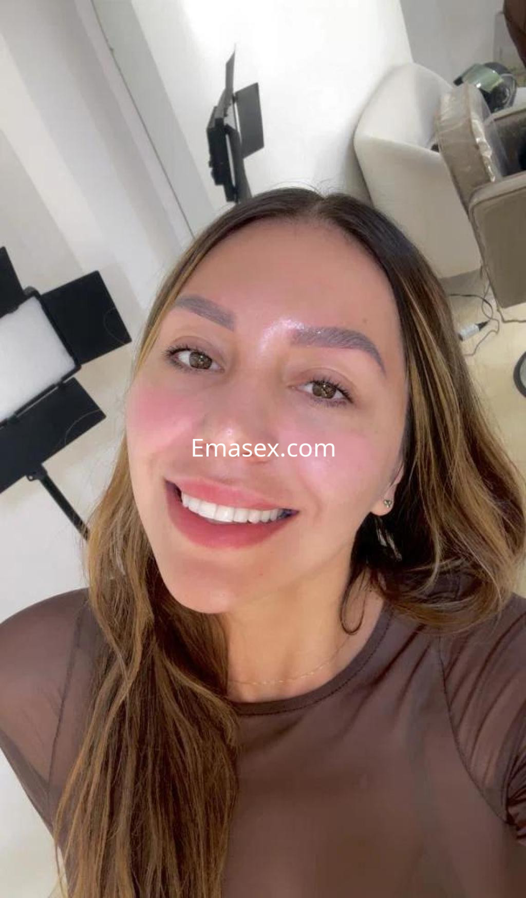 Puta sonríe a la cámara con cabello largo y suelto, vistiendo un top transparente en un entorno luminoso de Cáceres.