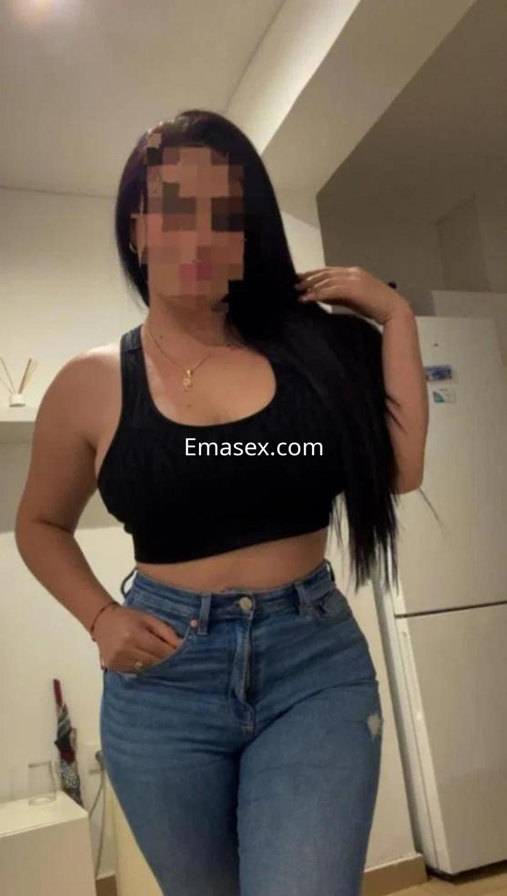 Escort en Castellón con cabello largo y lacio, vistiendo top negro y jeans ajustados, posando en un ambiente interior.