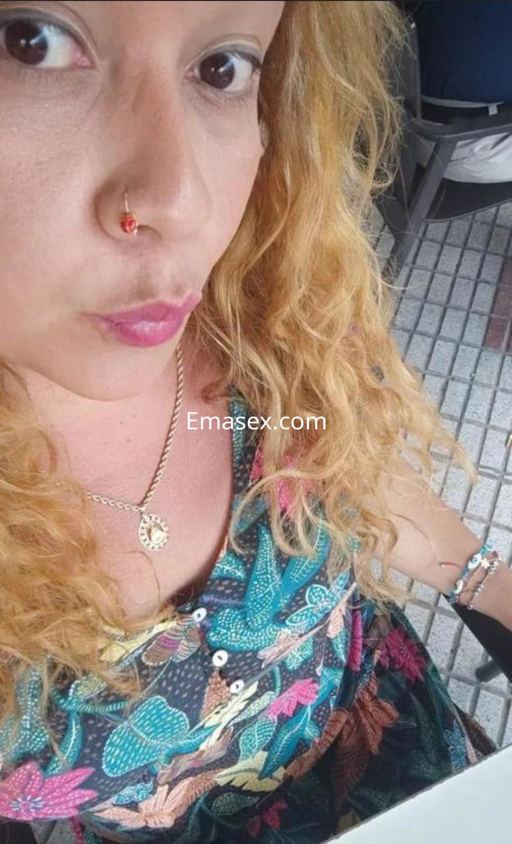 Escort con cabello rizado y rubio, viste una blusa colorida con estampado floral en Coruña.