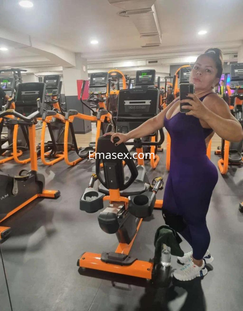La puta en Madrid posa en un gimnasio, vistiendo un ajustado conjunto deportivo morado y zapatillas blancas.