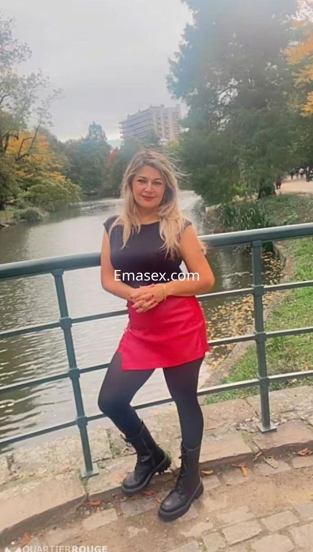 La puta posando con una blusa negra y falda roja en un parque de Vigo, junto a un lago.