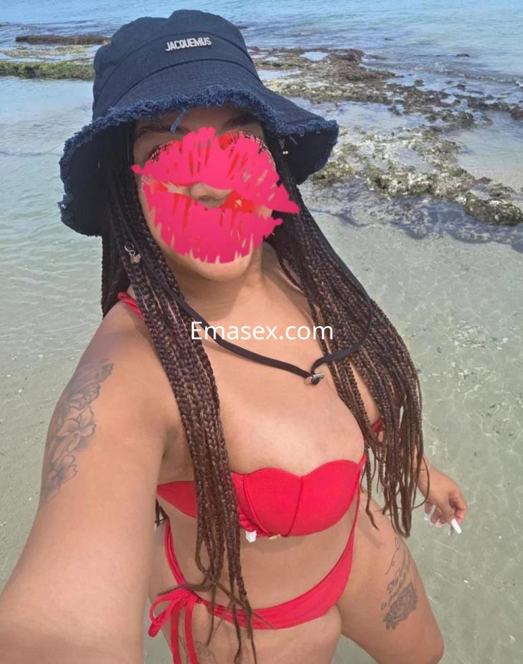 Escort en la playa de Valladolid, luciendo un bikini rojo y un sombrero negro, con trenzas largas.