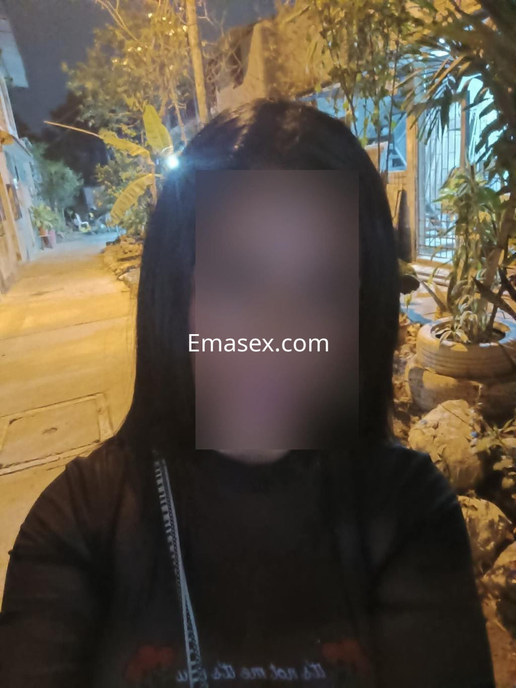 Puta con cabello largo y lacio, vestida con una camiseta negra, posando en una calle tranquila de Albacete.