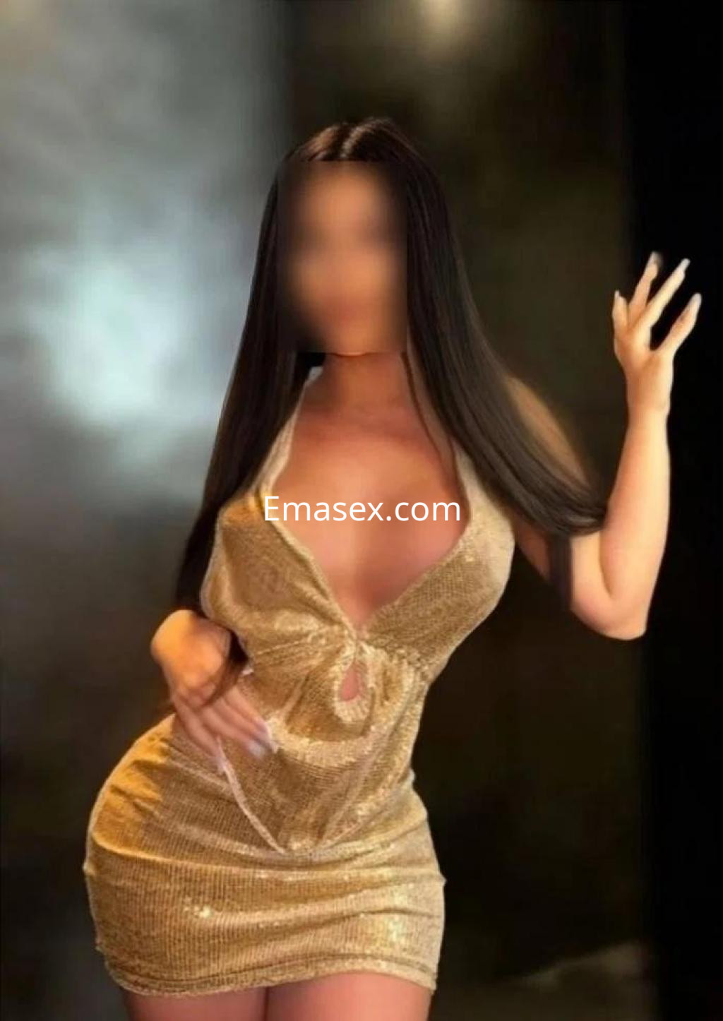 Escort en Badajoz, luce un vestido dorado con brillos y un escote pronunciado, posando con una mano levantada.