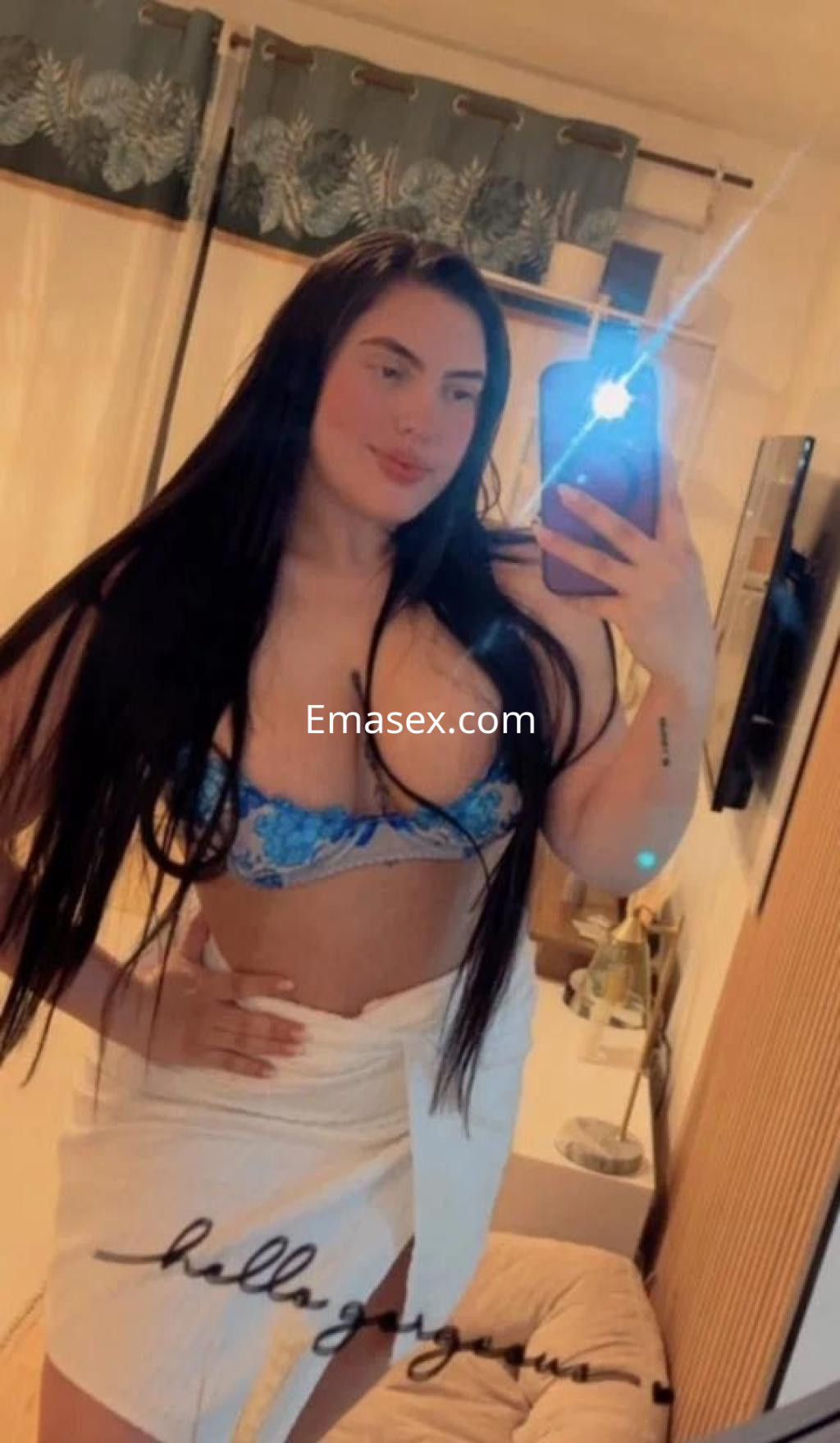 Escort en Barcelona se muestra en un espejo, con cabello largo y lacio, vistiendo un sujetador azul y una toalla.
