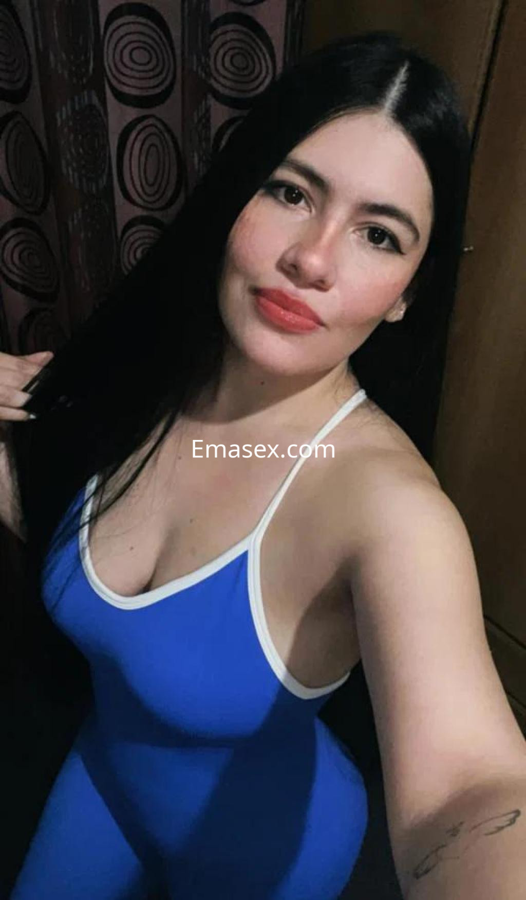 Escort en Girona con cabello largo y lacio, vistiendo un body azul que resalta su figura y sonríe a la cámara.