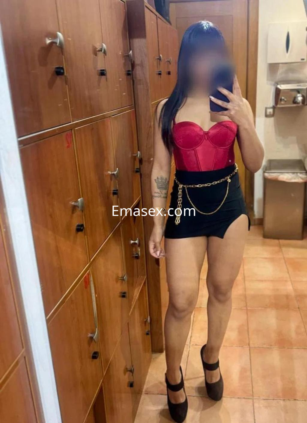 La puta en Lugo se muestra en un espejo con un corsé rojo y una falda corta negra, luciendo tacones altos.