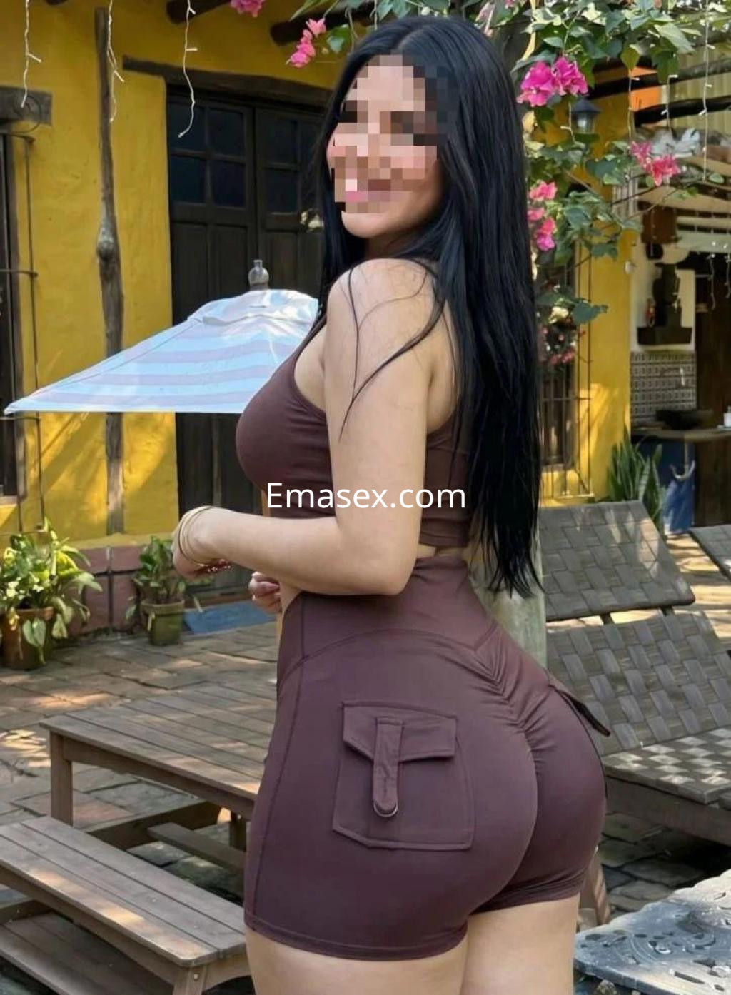 Escort en Lugo con cabello largo y oscuro, vistiendo un conjunto ajustado de color marrón en un entorno tropical.
