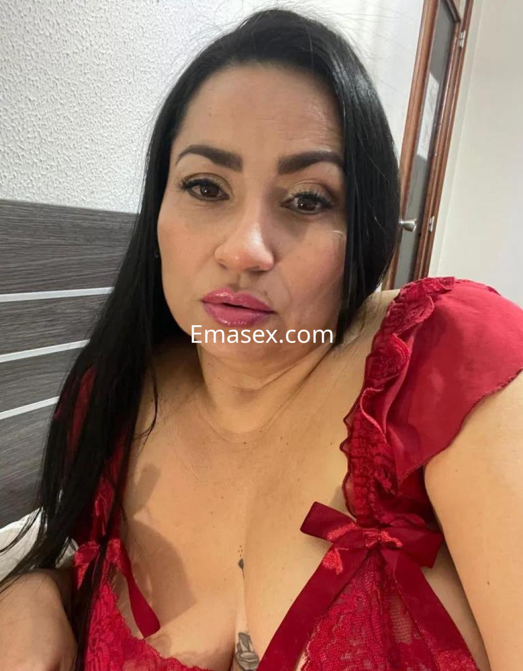 Escort en Lugo, con cabello largo y oscuro, viste un conjunto de lencería roja, posando de manera seductora.