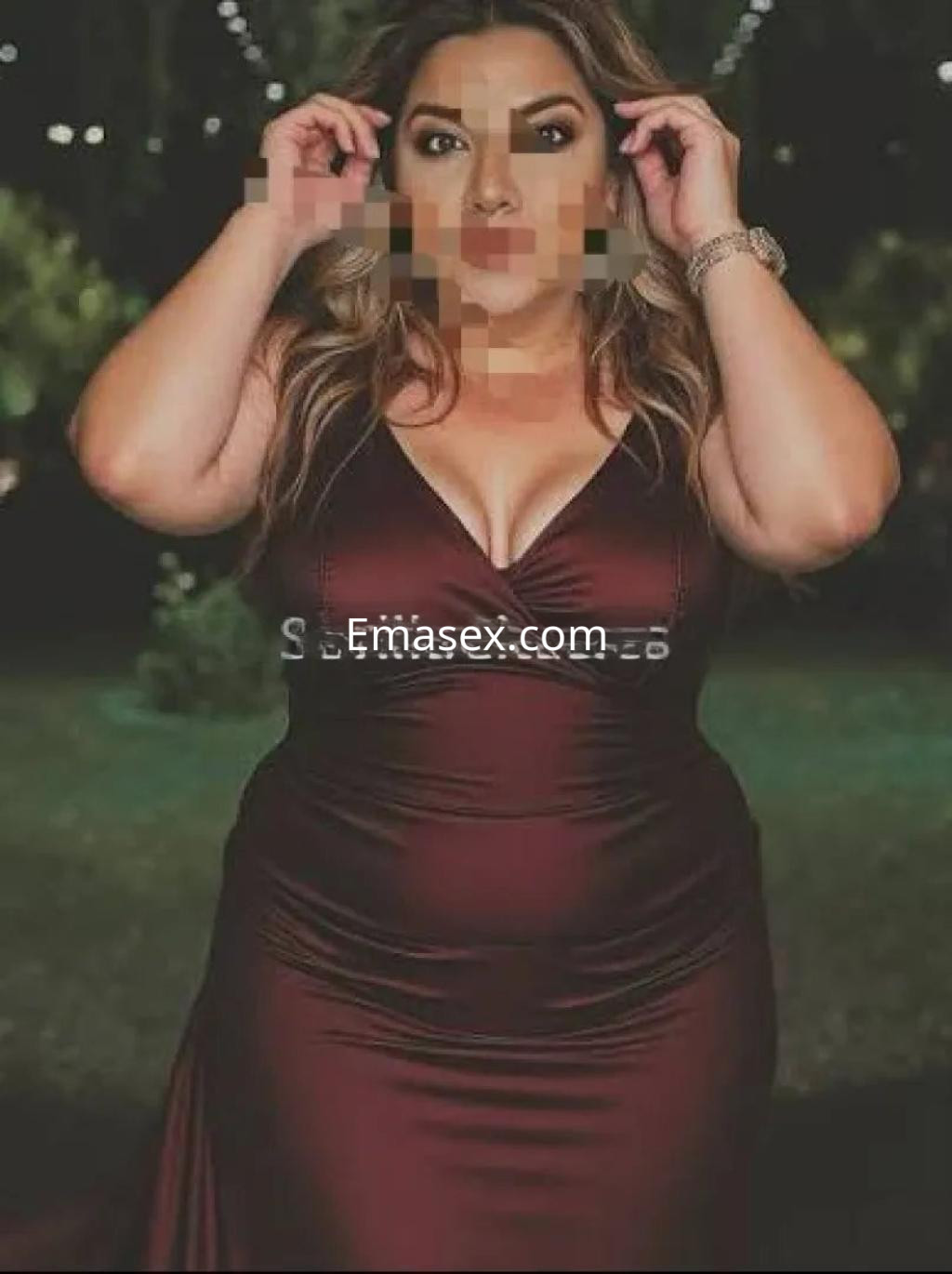 Escort en Sevilla con un vestido largo color burdeos, posando en un entorno iluminado al aire libre.