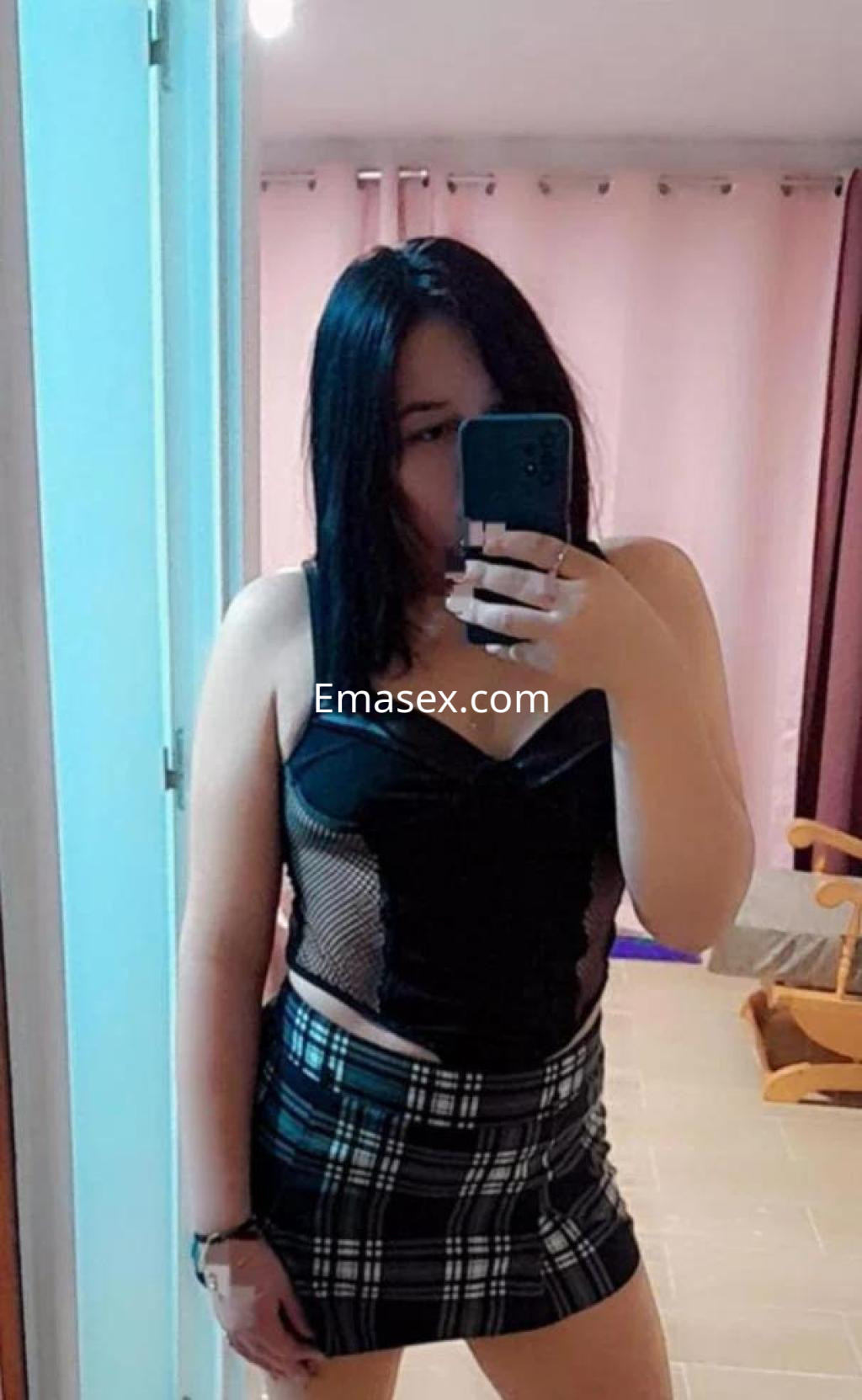 La puta posa frente al espejo en Zaragoza con una blusa negra y una falda corta de cuadros.
