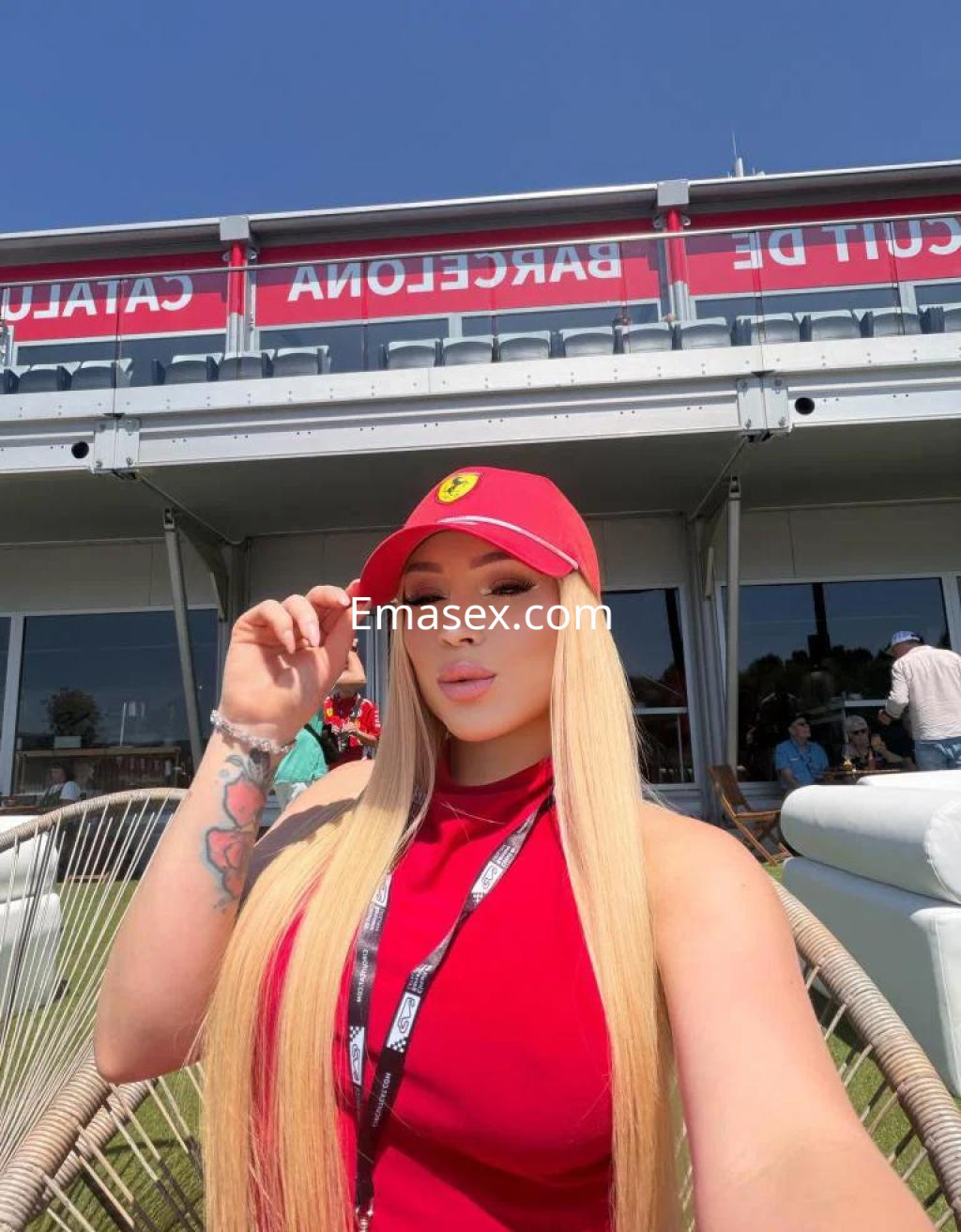 Escort en Barcelona con cabello largo y rubio, vistiendo un vestido rojo, posando con una gorra en un ambiente al aire libre.