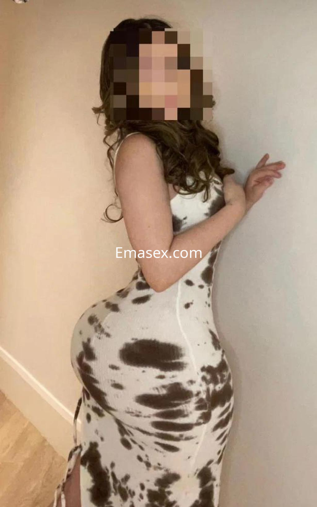 Escort posando de perfil en Girona, luciendo un vestido ajustado de estampado marrón y blanco.