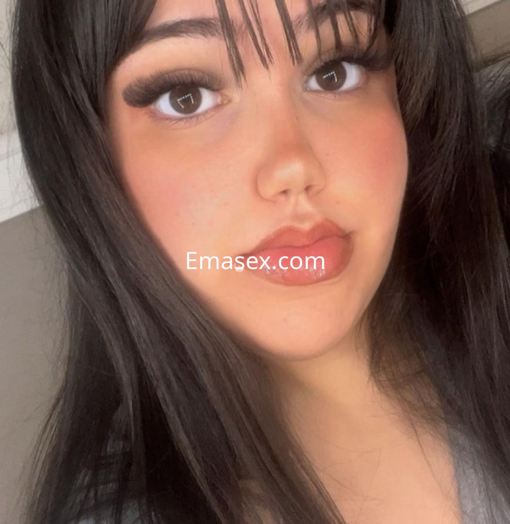 Escort en Málaga con cabello largo y oscuro, mirada intensa y labios destacados, posando en un ambiente interior.