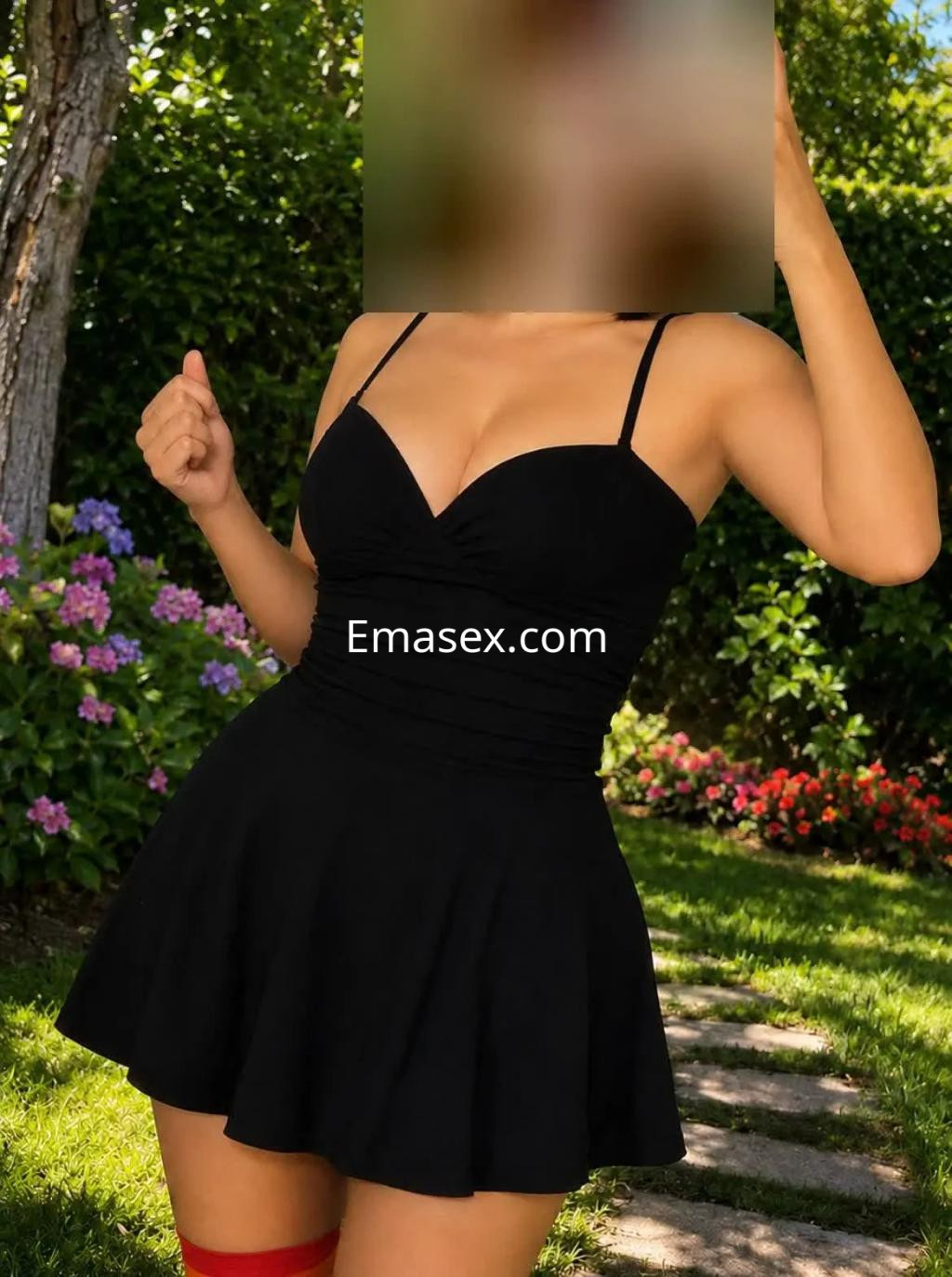 Puta en Zaragoza vistiendo un vestido negro ajustado con tirantes, posando en un jardín con flores.