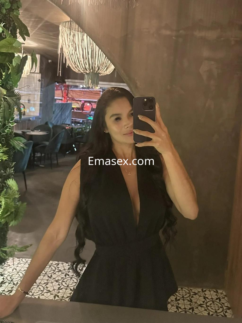 Escort en Alicante con cabello largo y oscuro, vestida con un elegante mono negro, posando frente a un espejo.