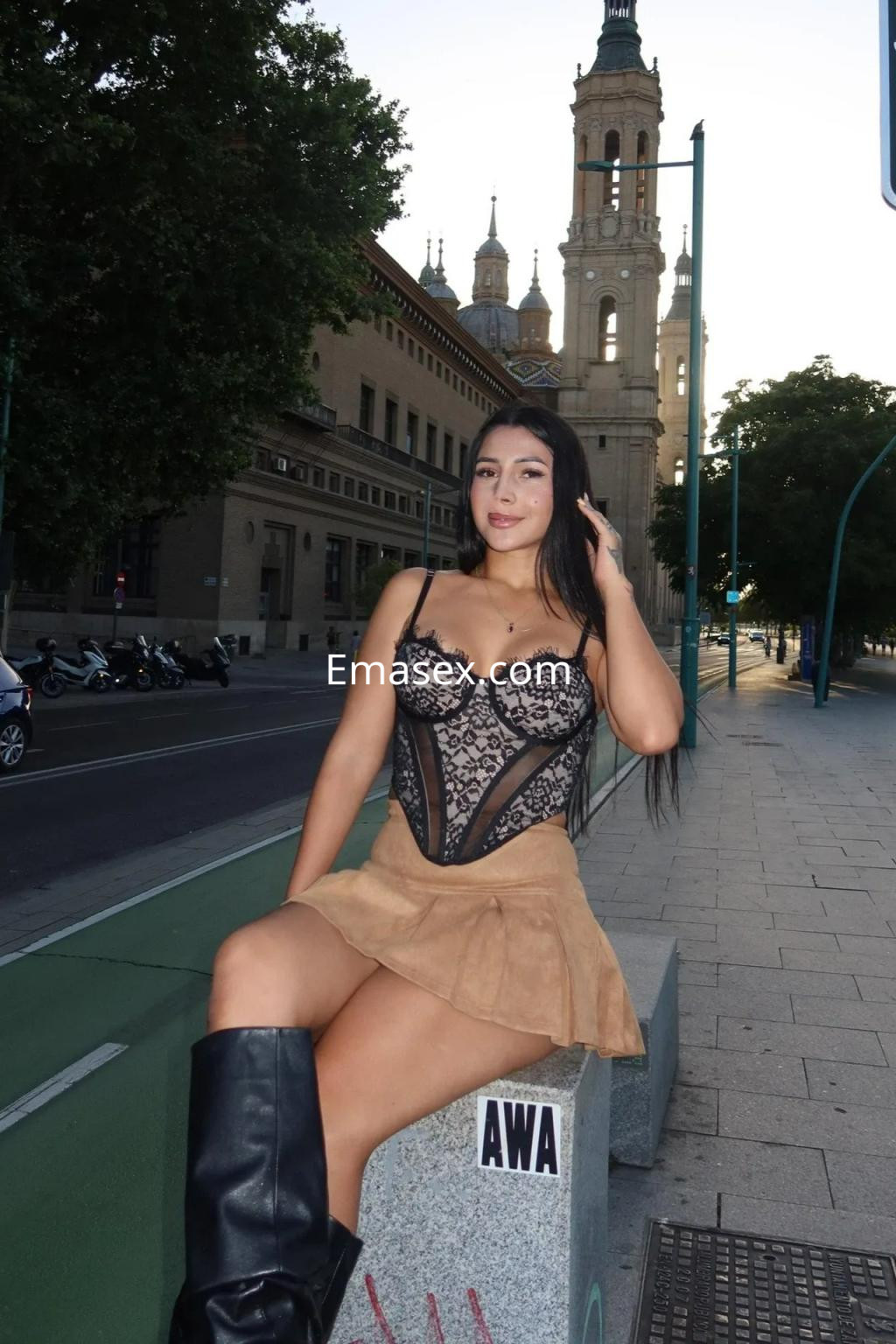 Puta en Zaragoza, luciendo un body de encaje y una falda corta de color marrón, sentada en una banca.