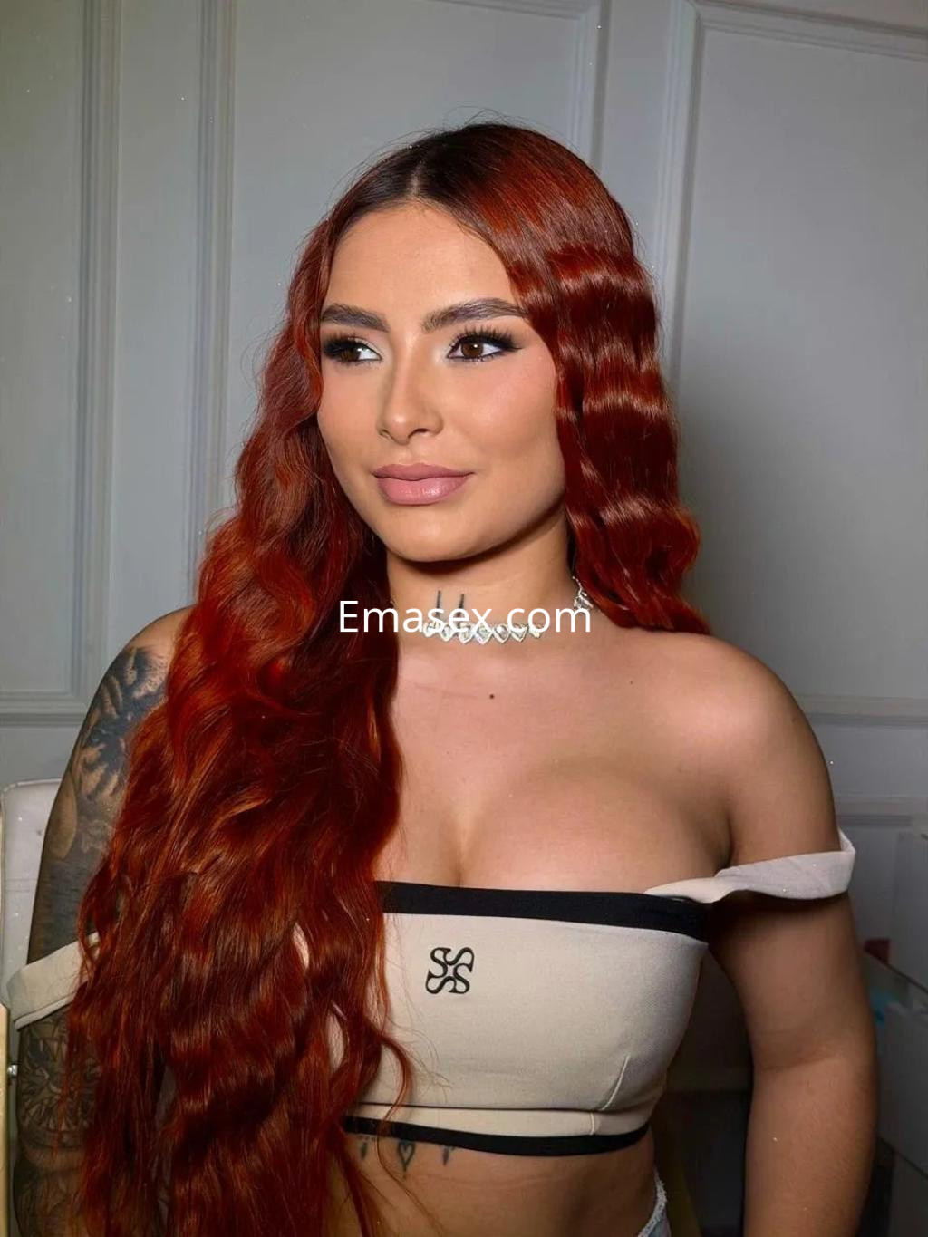 Puta de cabello largo y ondulado en tonos rojos, viste un top ajustado en Alicante, luciendo una expresión confiada.