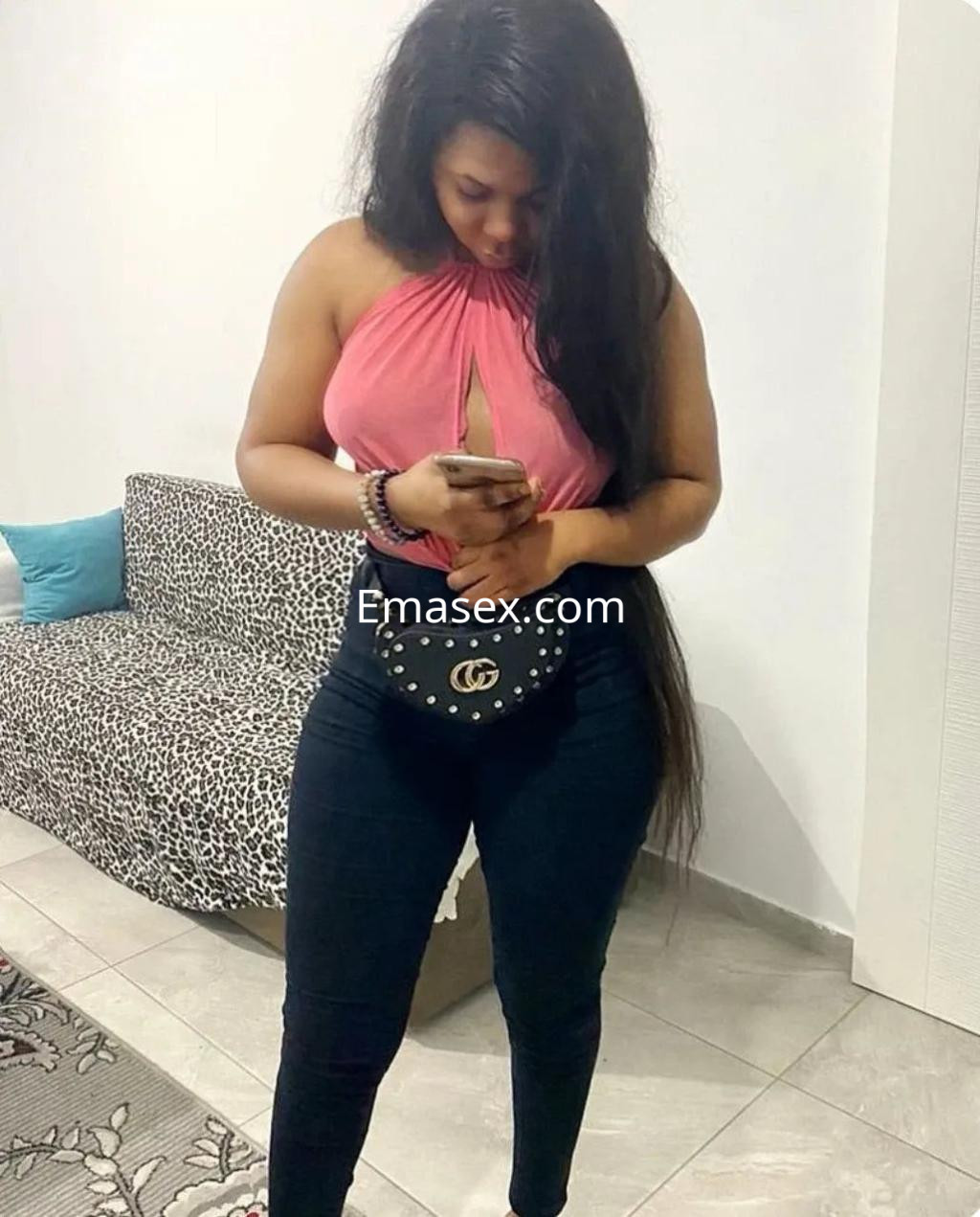 Escort en Alicante con cabello largo y oscuro, vestida con blusa rosa y pantalones ajustados, revisando su teléfono.