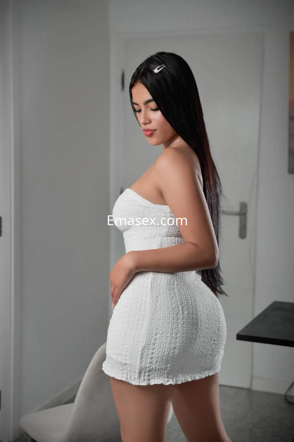 Escort en Alicante viste un vestido blanco ajustado y se gira ligeramente, mostrando su cabello largo y lacio.