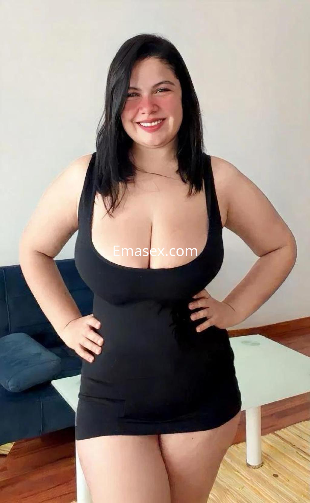 Escort en Barcelona con cabello oscuro, vestido negro ajustado, sonriendo y posando en un ambiente interior.