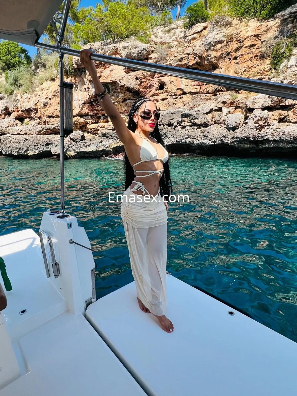 Puta posando en un yate en Cádiz, con un conjunto de bikini blanco y pantalones largos, luciendo gafas de sol.