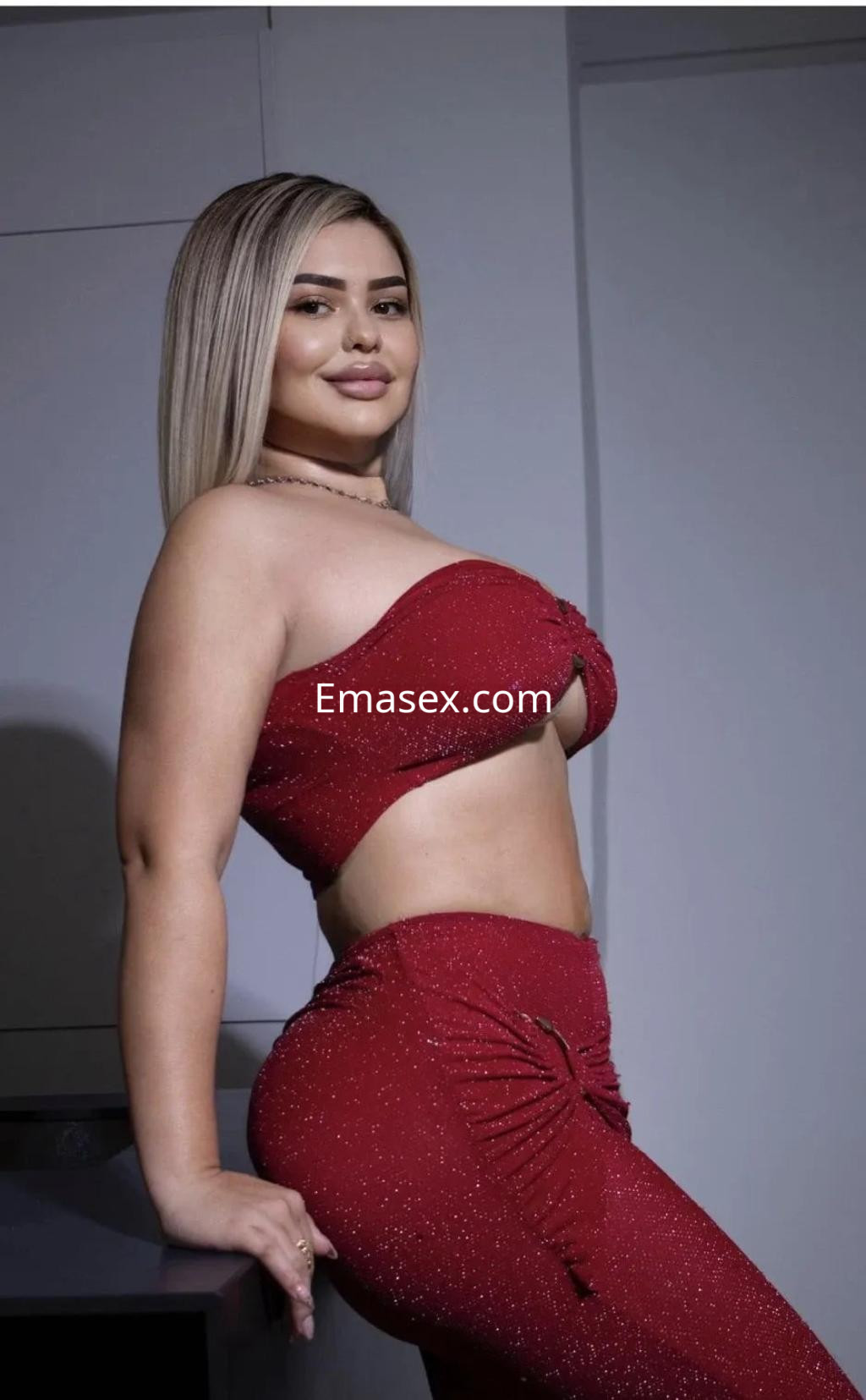Escort en Cádiz posando con un conjunto rojo brillante, que destaca su figura, en un ambiente moderno y elegante.