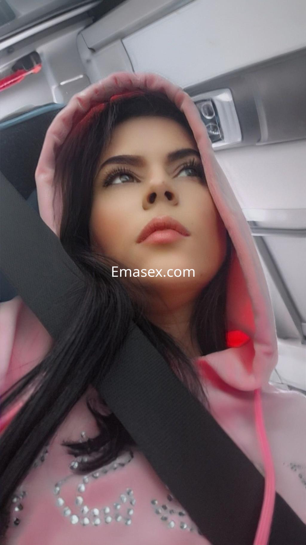 Escort con sudadera rosa y capucha, sentada en un vehículo, mirando hacia arriba en Granada.