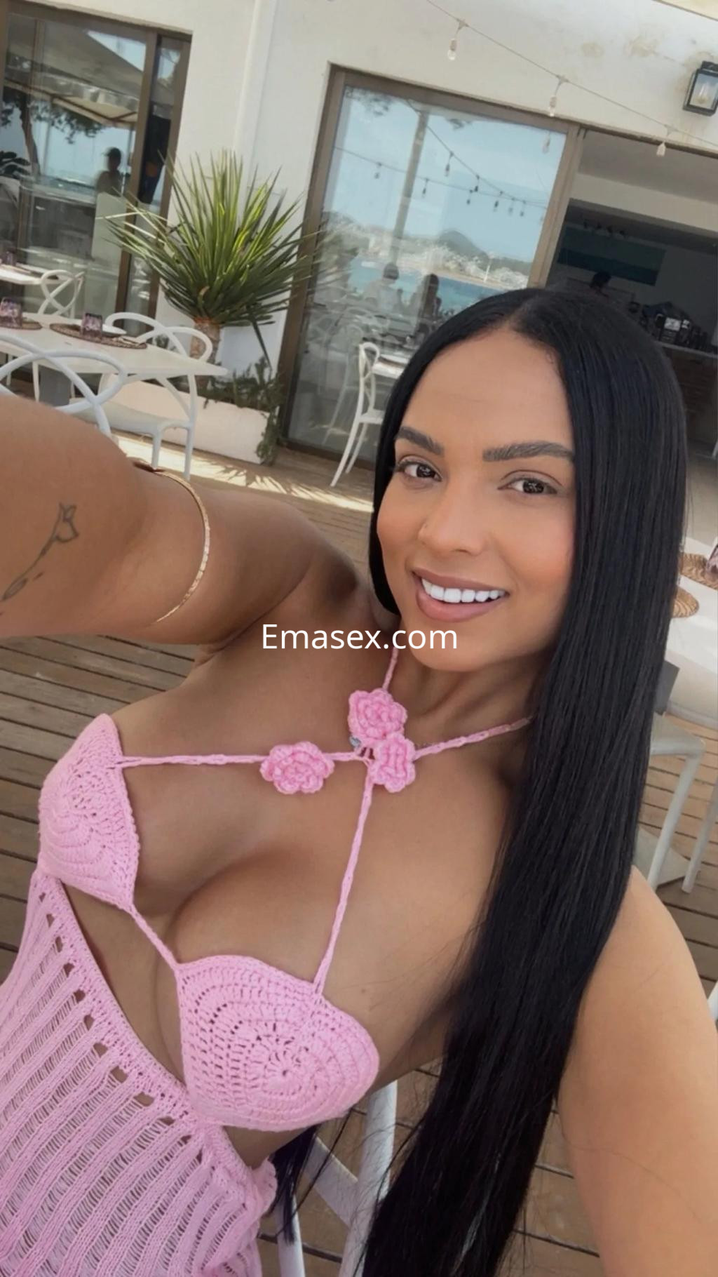 La escort en Málaga luce un vestido de crochet rosa que resalta su figura y largo cabello negro mientras sonríe.