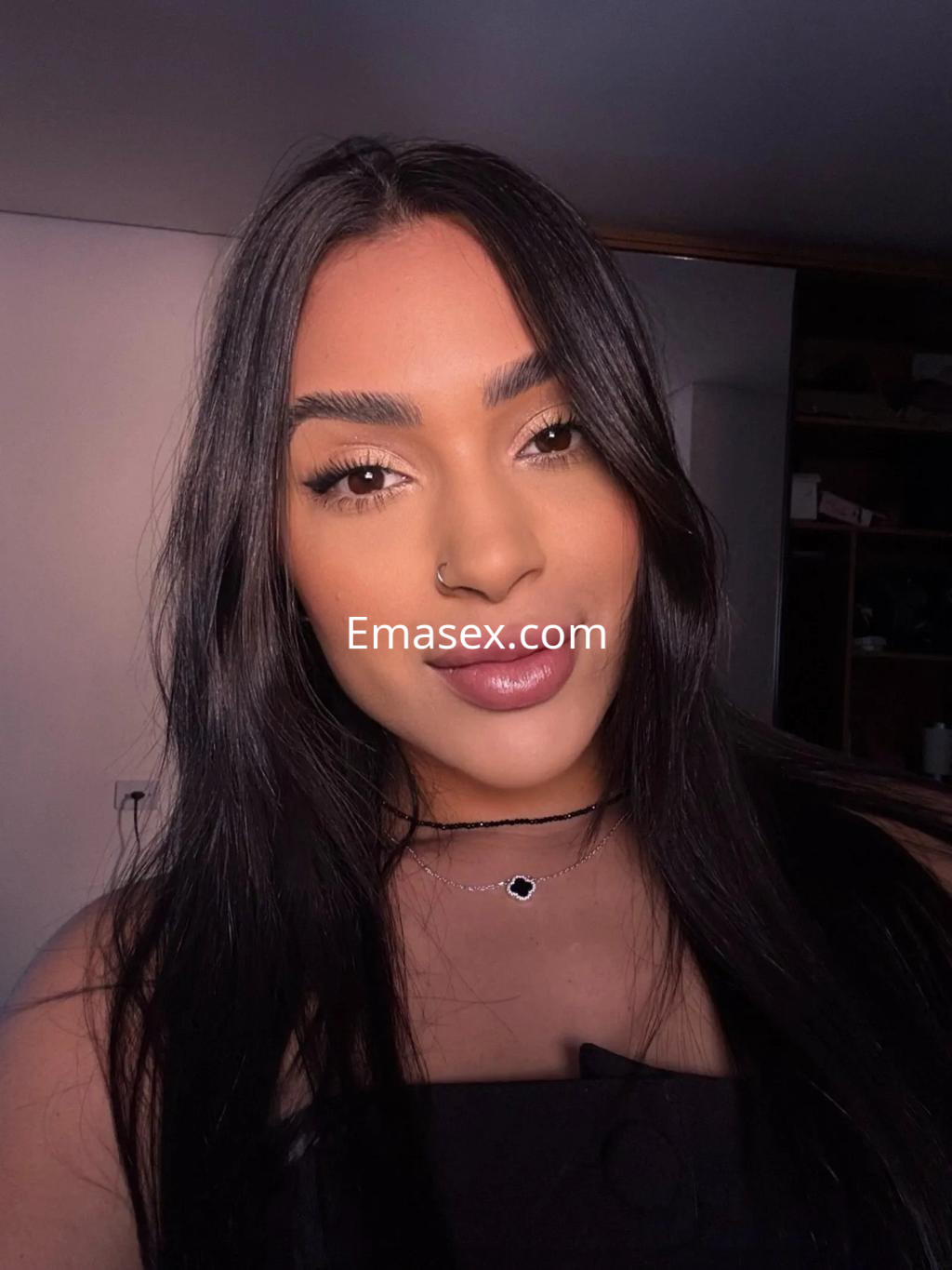 Puta en Málaga con cabello largo y oscuro, luciendo un maquillaje natural y un collar delgado en un fondo sencillo.
