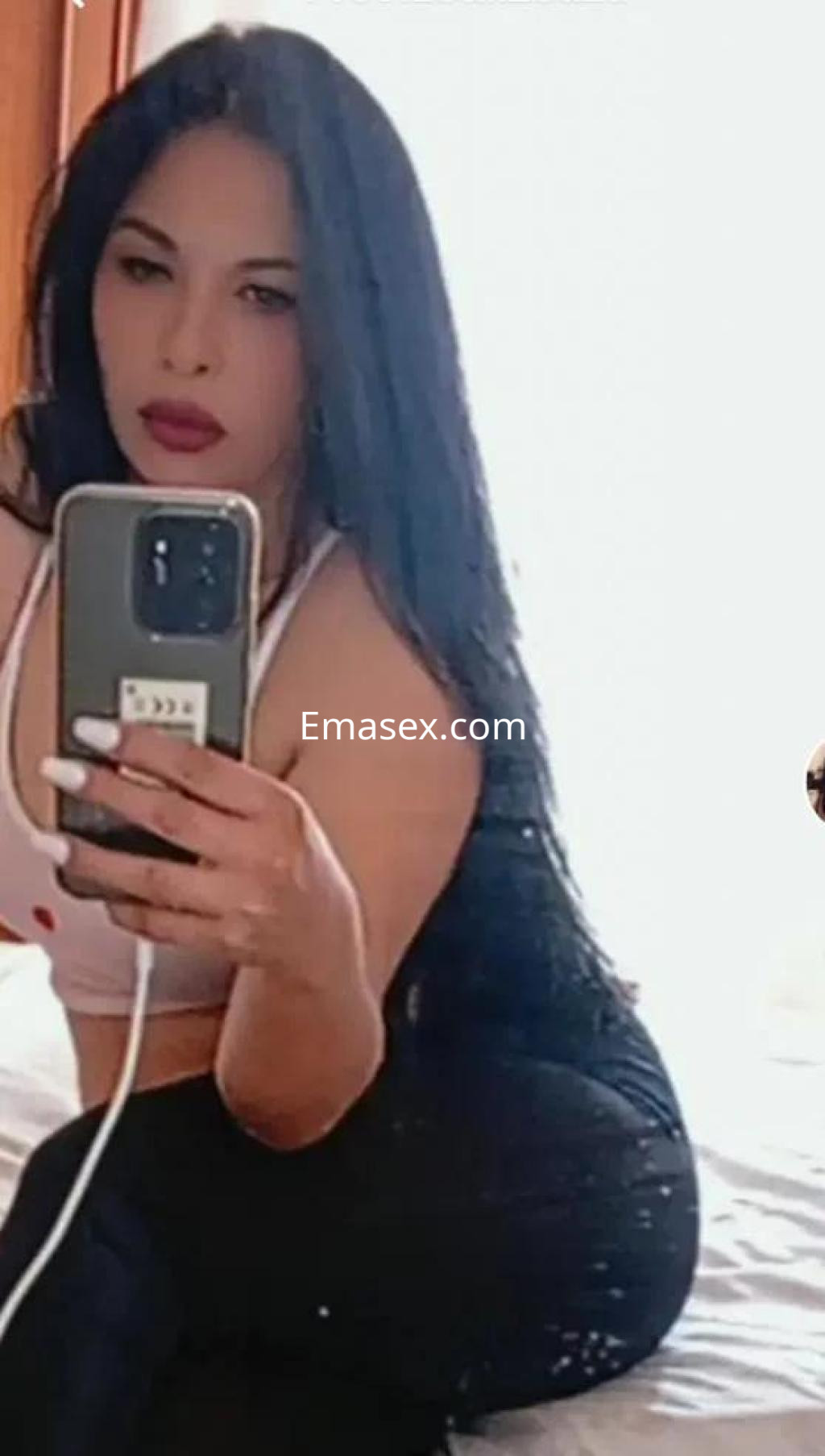 Puta de Gijón posando con top blanco y pantalón negro, mostrando su cabello largo y sedoso mientras se mira al espejo.