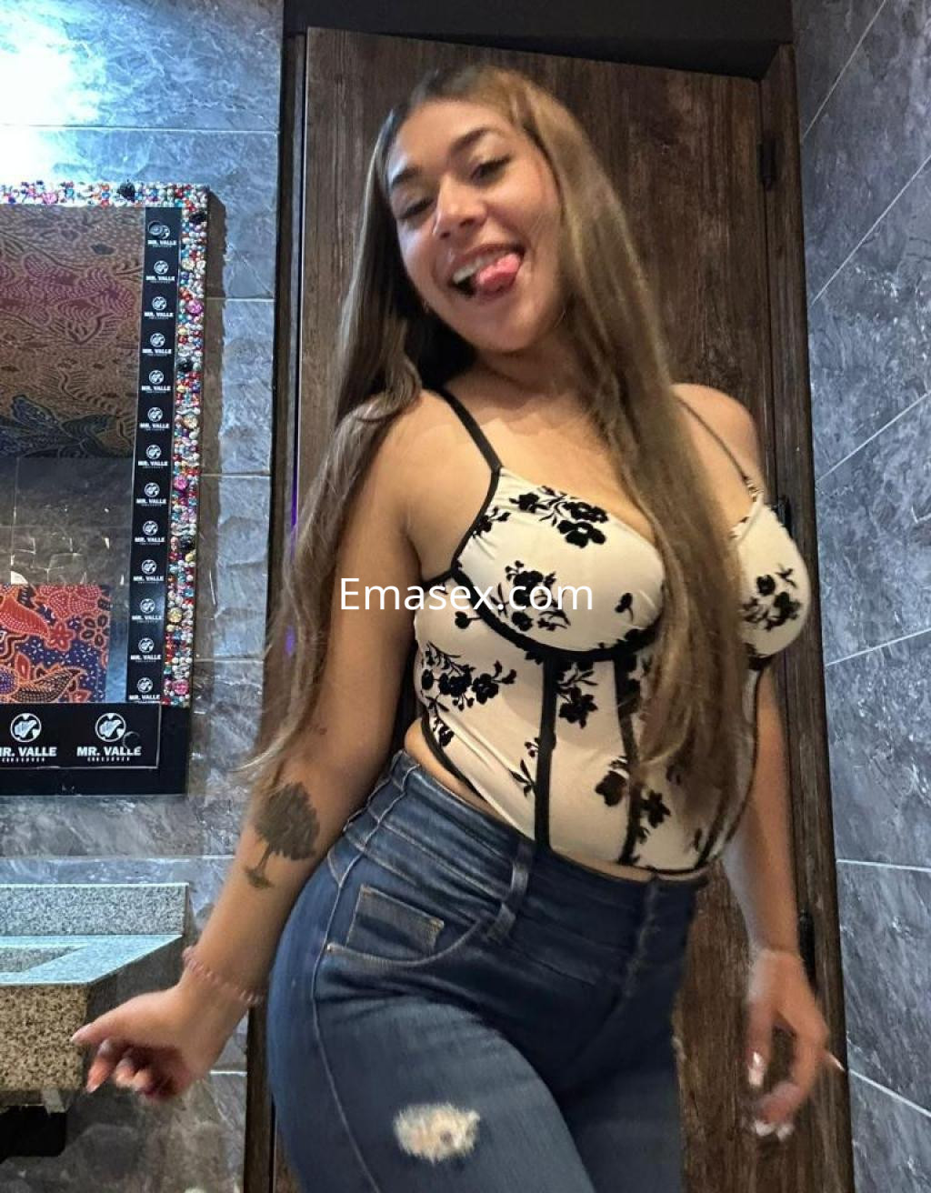 Escort en Pontevedra posando con un body de flores y jeans ajustados, mostrando una sonrisa juguetona.