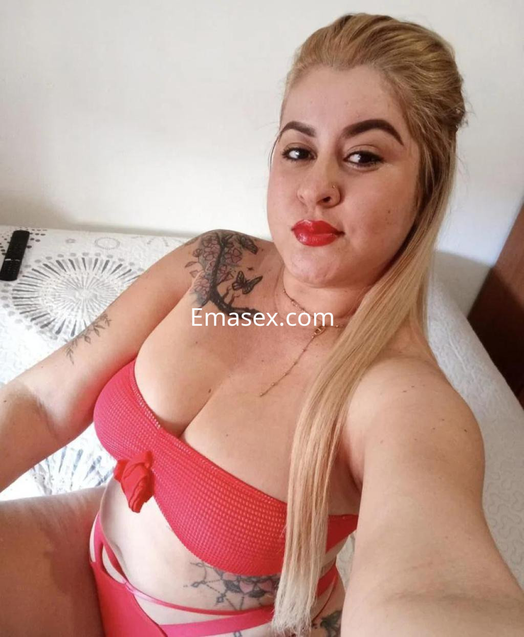 Escort en Salamanca posando con un top rojo y braguita a juego, mostrando su cabello rubio y tatuajes.